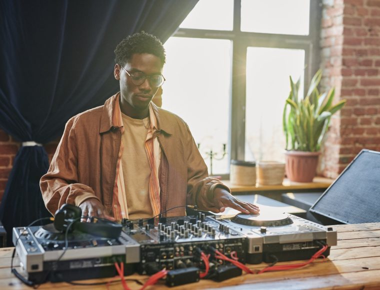 Young serious black man looking at dj board while touching turntables